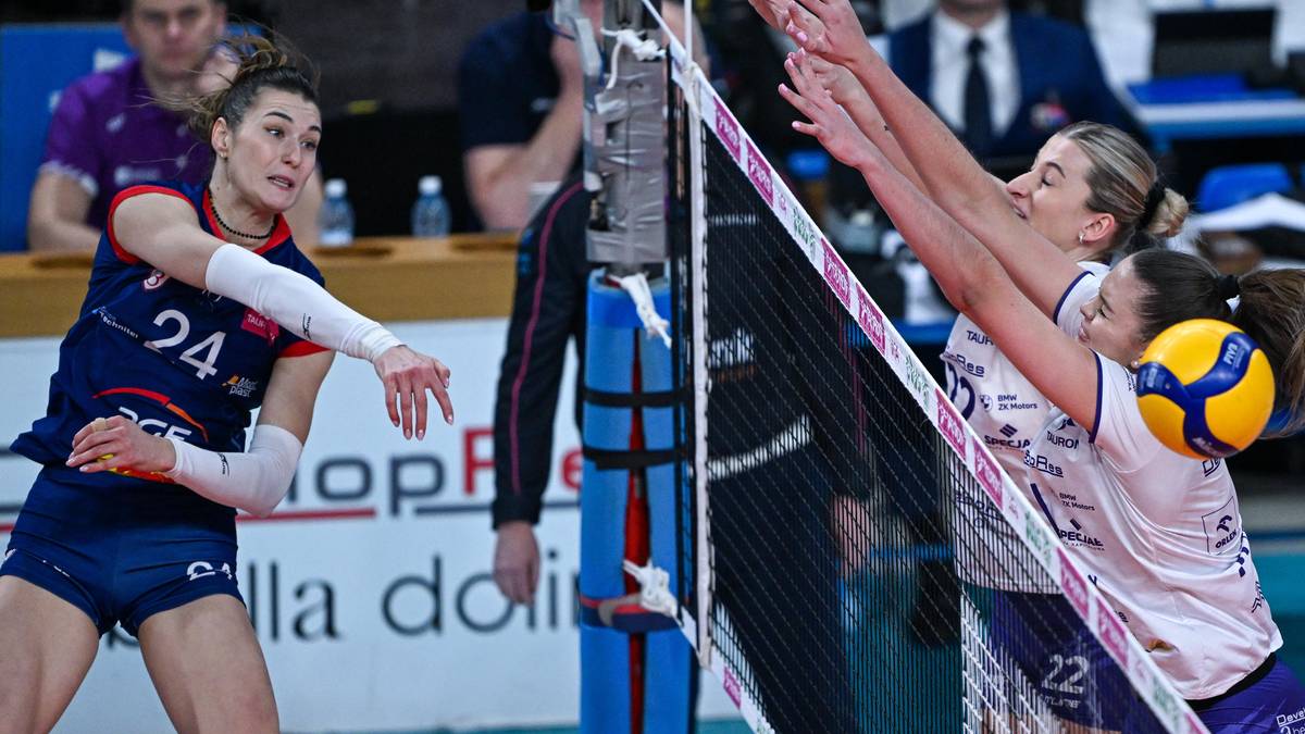 Dwie siatkarki rywalizują przy siatce, jedna z nich pr&oacute;buje zablokować atak lub odbić piłkę.