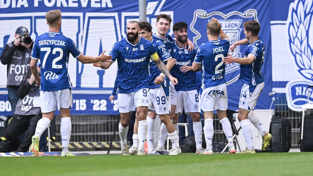 Piłkarze Lecha Poznań w niebieskich strojach cieszą się po zdobyciu bramki na boisku, z kibicami na trybunach w tle.