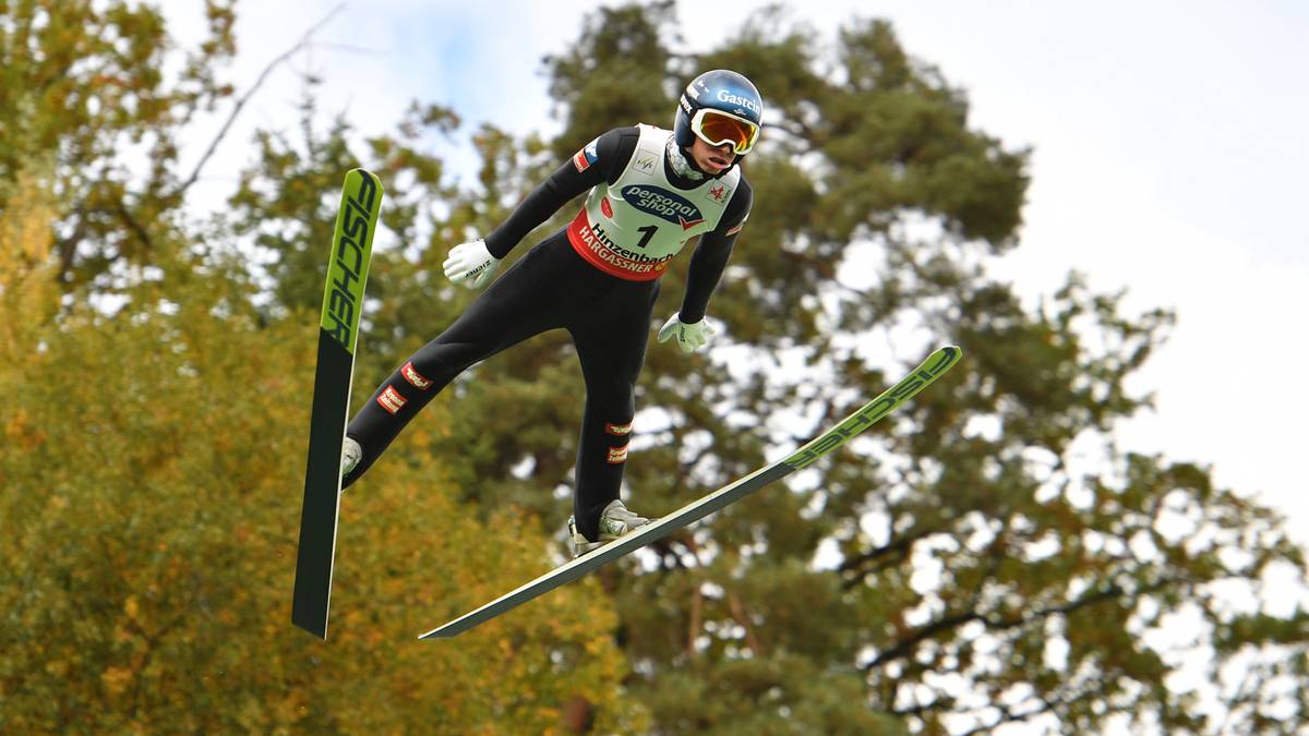 Skoczek narciarski w locie na tle drzew i nieba.