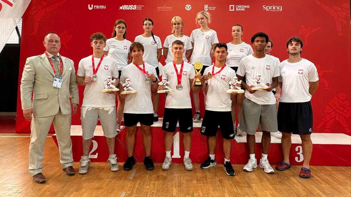 Grupa młodych sportowc&oacute;w z nagrodami na podium, obok nich stoi mężczyzna w garniturze wręczający trofea.