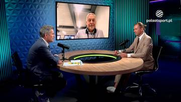 Dw&oacute;ch mężczyzn siedzi przy okrągłym stole w studio telewizyjnym. Na ekranie nad nimi wyświetla się twarz trzeciego mężczyzny.