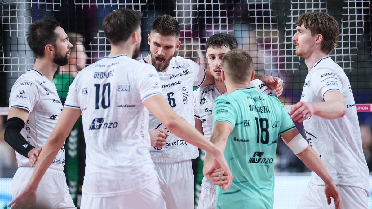 Sześciu siatkarzy w białych i zielonych koszulkach stoi w grupie, rozmawiając i gestykulując. Jeden z nich, w zielonej koszulce z numerem 18, jest zwrócony tyłem do widza.