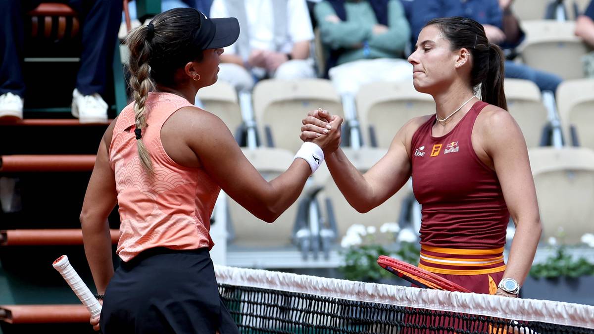 Dwie tenisistki podają sobie ręce nad siatką po meczu. Jedna w pomarańczowej koszulce i czarnej spódniczce, druga w bordowej sukience sportowej.