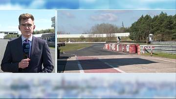 Mężczyzna w garniturze trzyma mikrofon i m&oacute;wi, obok widok pustego toru wyścigowego z barierkami.