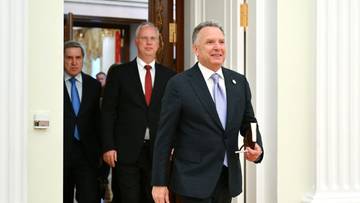 Trzech mężczyzn w garniturach wchodzi do pomieszczenia.