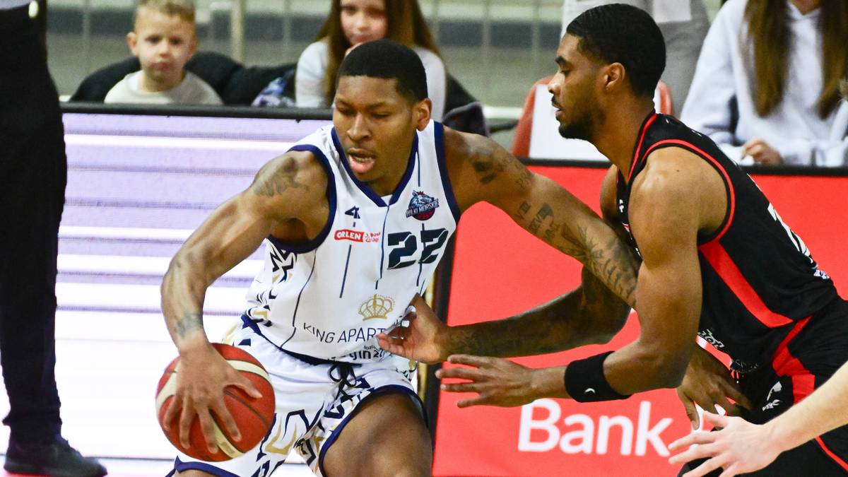 Gracz w białej koszulce z numerem 22 na plecach drybluje piłką do koszyk&oacute;wki, podczas gdy gracz w czarnej koszulce pr&oacute;buje go kryć.