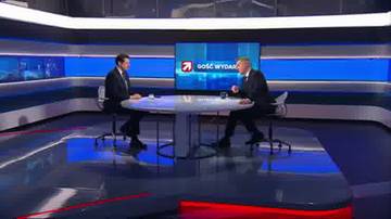 Dw&oacute;ch mężczyzn w garniturach siedzi naprzeciwko siebie przy okrągłym stole w studiu telewizyjnym. Na ekranie za nimi wyświetlany jest logotyp programu.