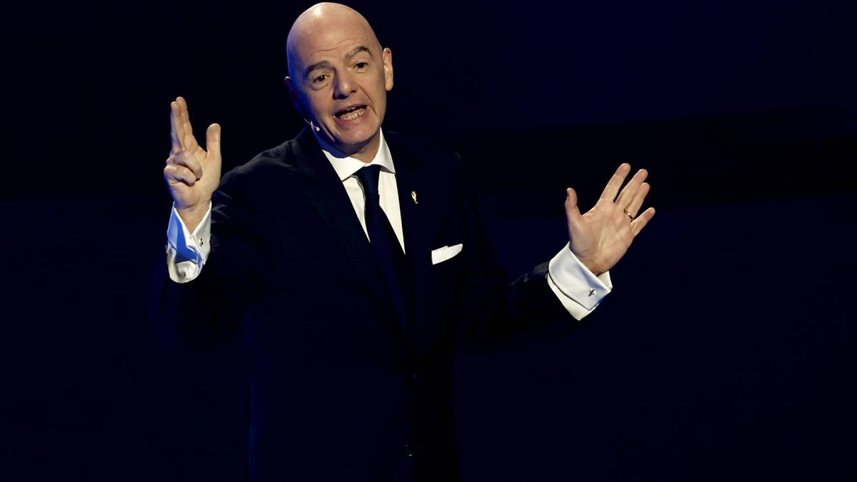 Mężczyzna w garniturze gestykuluje obiema rękami, wskazując dwoma palcami lewej dłoni.