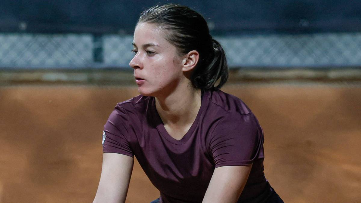 Kobieta w trakcie gry w tenisa, trzyma rakietę i piłkę.