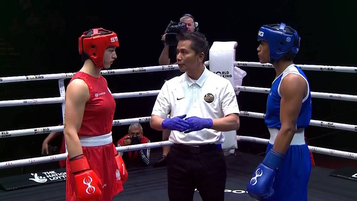 Dwóch bokserów, kobieta w czerwonym stroju i kobieta w niebieskim stroju, stoi na ringu bokserskim przed arbitrem.