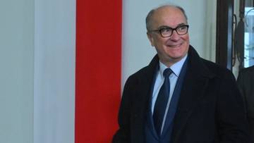 Mężczyzna w eleganckim stroju, w okularach, uśmiecha się.