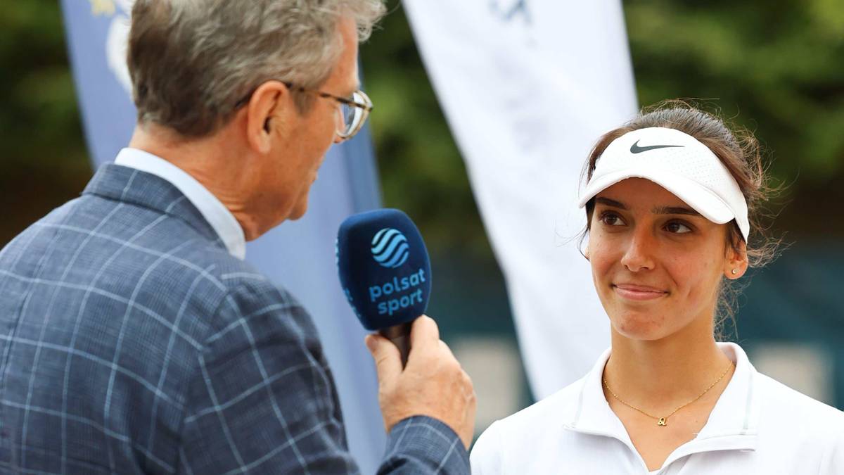 Mężczyzna w okularach i marynarce, trzymający mikrofon Polsat Sport, rozmawia z młodą kobietą w białej czapce z daszkiem i stroju sportowym.