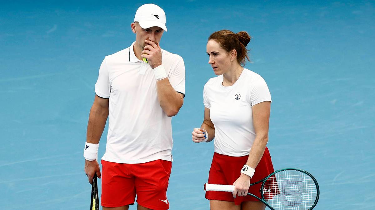 Mężczyzna i kobieta w strojach tenisowych idą po korcie z rakietami.