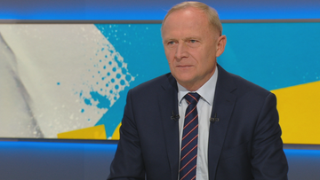 Mężczyzna w garniturze siedzi w studiu telewizyjnym.