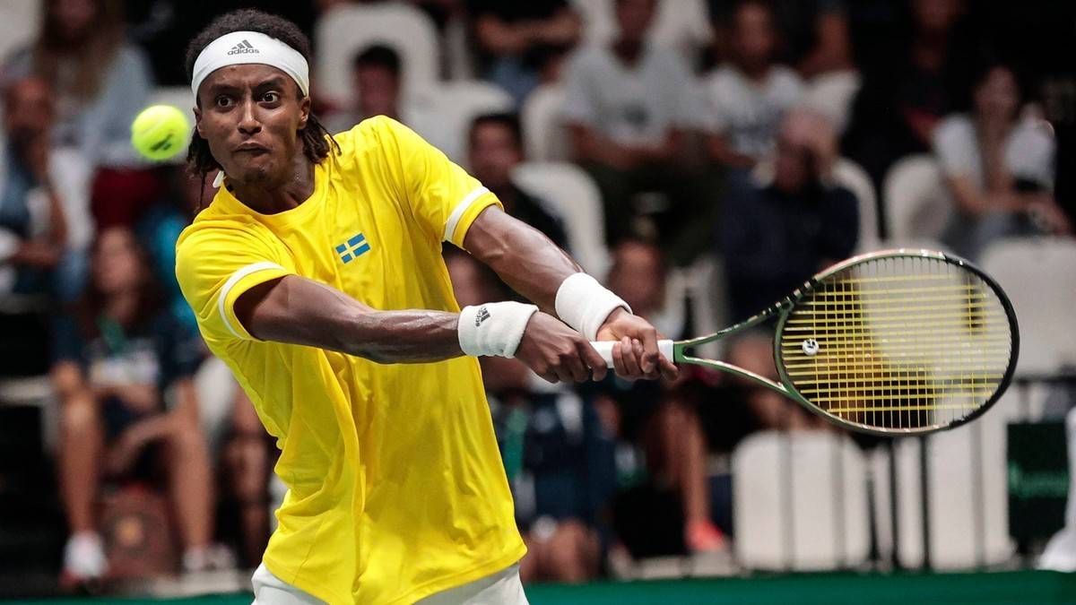 Tenisista w żółtej koszulce z flagą Szwecji uderza piłkę forhendem.