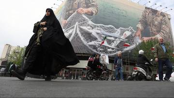 Kobieta w czarnym hidżabie przechodzi obok wielkiego muralu przedstawiającego fragmenty wojskowego umundurowania i symboli marynarki wojennej.