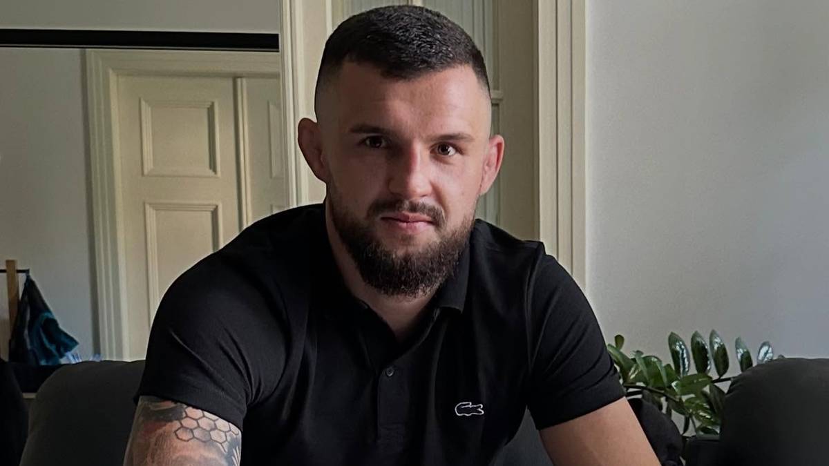 Mężczyzna w czarnej koszulce i jeansach siedzi przy drewnianym stole, przeglądając dokumenty.