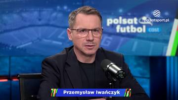 Mężczyzna w okularach i czarnym garniturze siedzi przed mikrofonem w studiu telewizyjnym. Na ekranie w tle widnieje logo "Polsat Futbol Cast" i fragment stadionu.