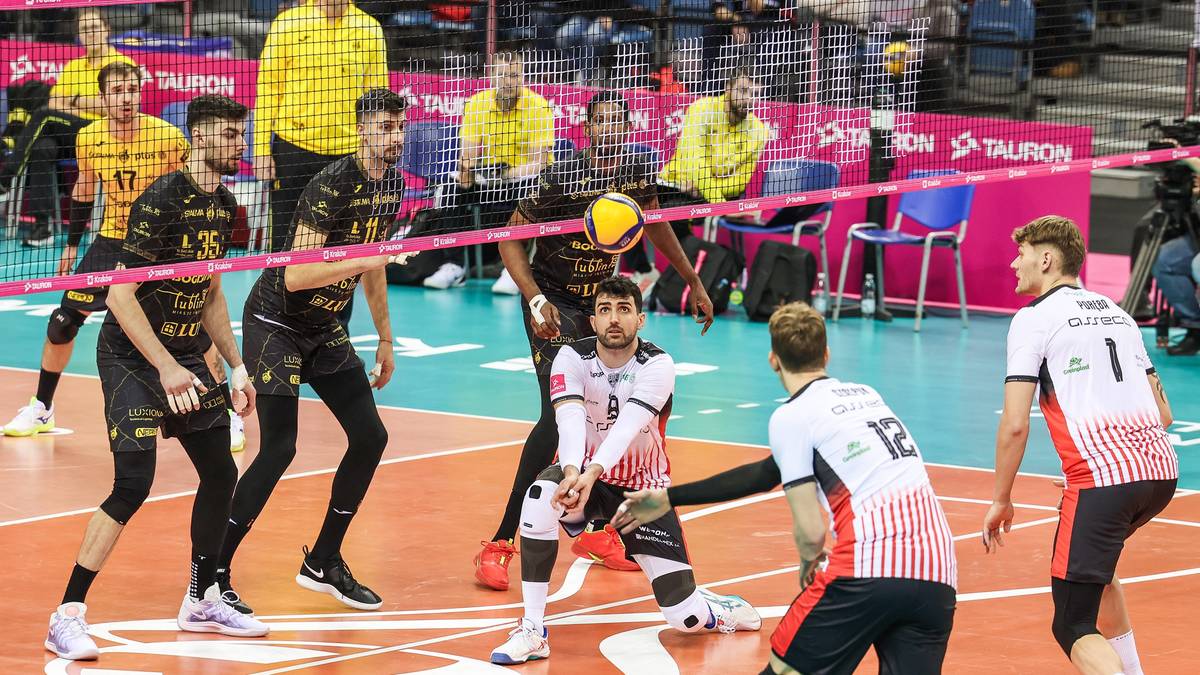 Siatkarze w akcji podczas meczu, z widoczną siatką i piłką.