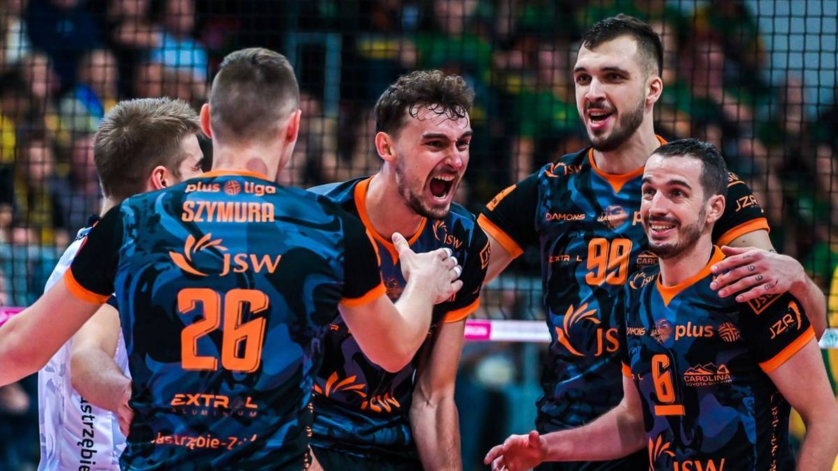 Grupa siatkarzy w strojach drużynowych cieszy się na boisku. Siatkarze Jastrzębskiego Węgla celebrują zwycięstwo.