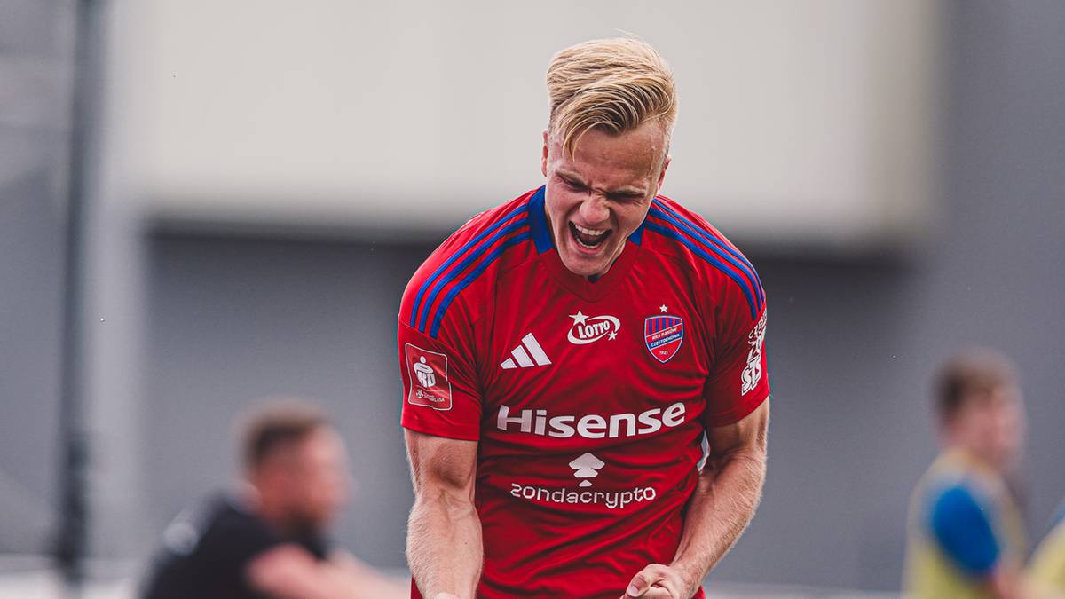 Piłkarz w czerwonej koszulce z niebieskimi pasami na ramionach, z zaciśniętą pięścią i wykrzywioną w okrzyku twarzą.