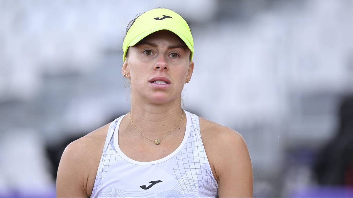 Tenisistka w ż&oacute;łtej czapce i białym stroju sportowym, patrząca przed siebie z wyrazem skupienia na twarzy.