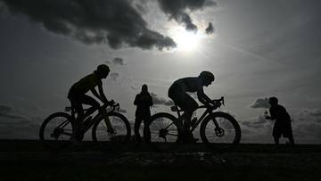 Sylwetki kolarzy na tle zachodzącego słońca.