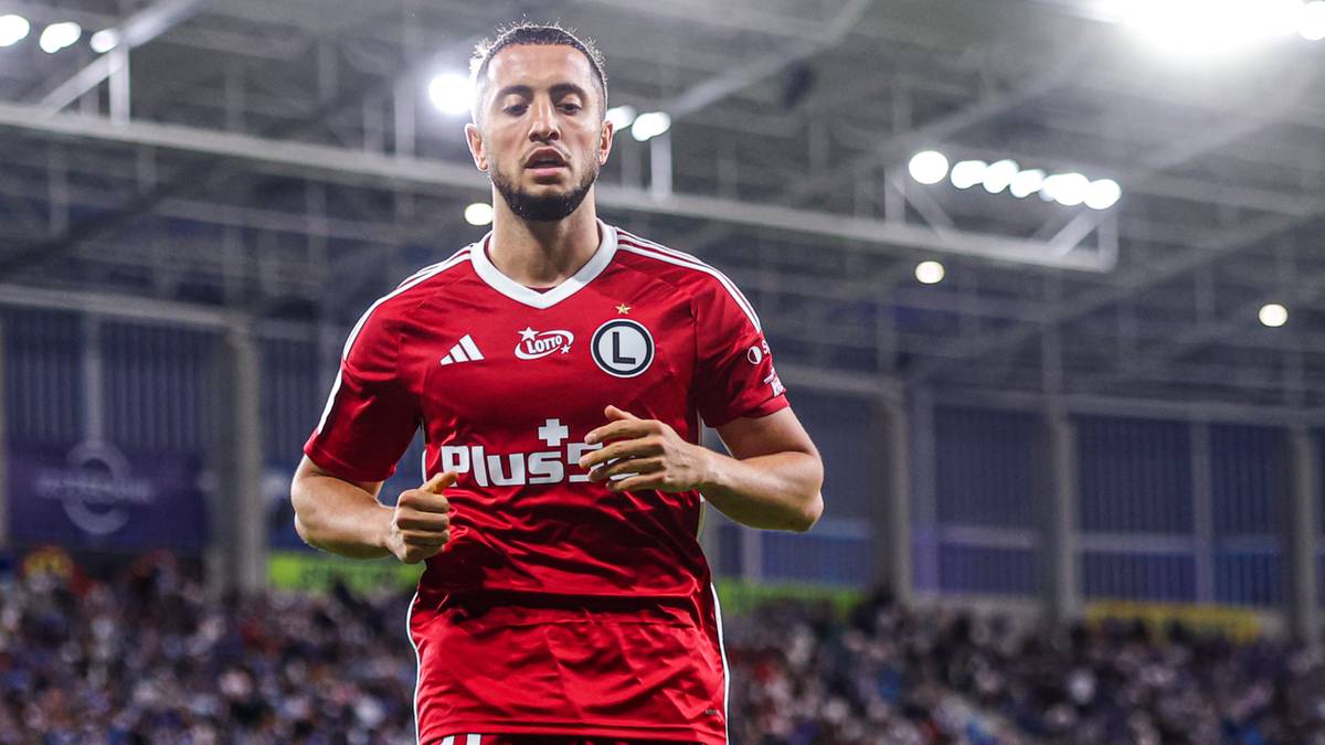 Piłkarz Legii Warszawa w czerwonej koszulce z białym kołnierzykiem biegnie po boisku.