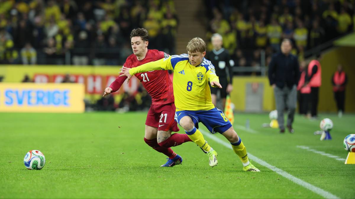 Dw&oacute;ch piłkarzy w akcji podczas meczu piłki nożnej, jeden w czerwonej koszulce, drugi w ż&oacute;łtej.