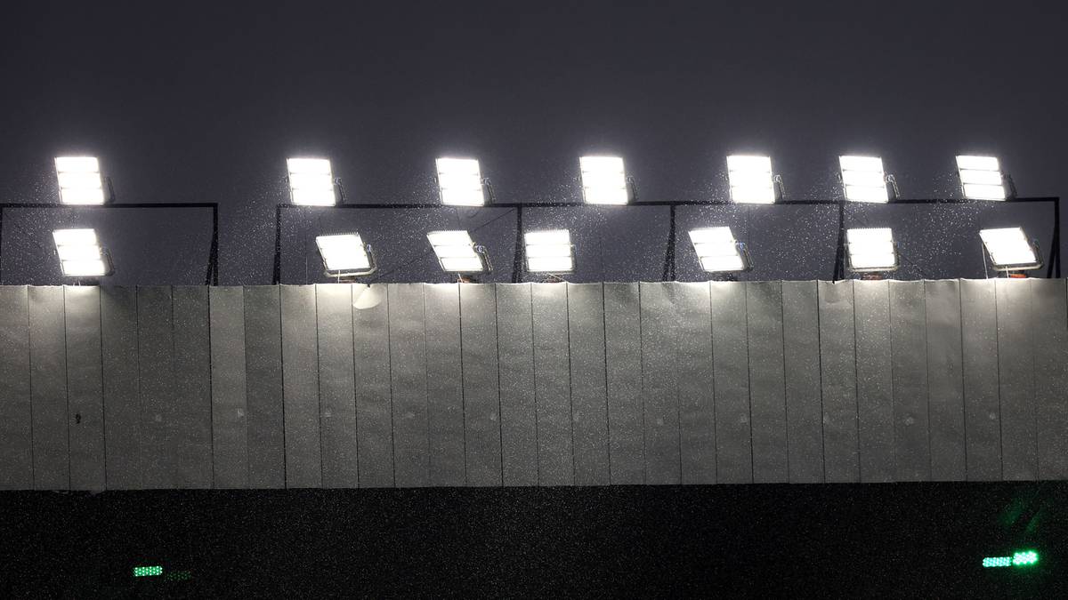 Rzędy jasnych reflektorów oświetlają betonowy mur stadionu w nocy.