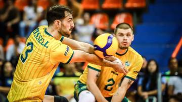 Dw&oacute;ch siatkarzy w ż&oacute;łtych koszulkach pr&oacute;buje odbić piłkę.