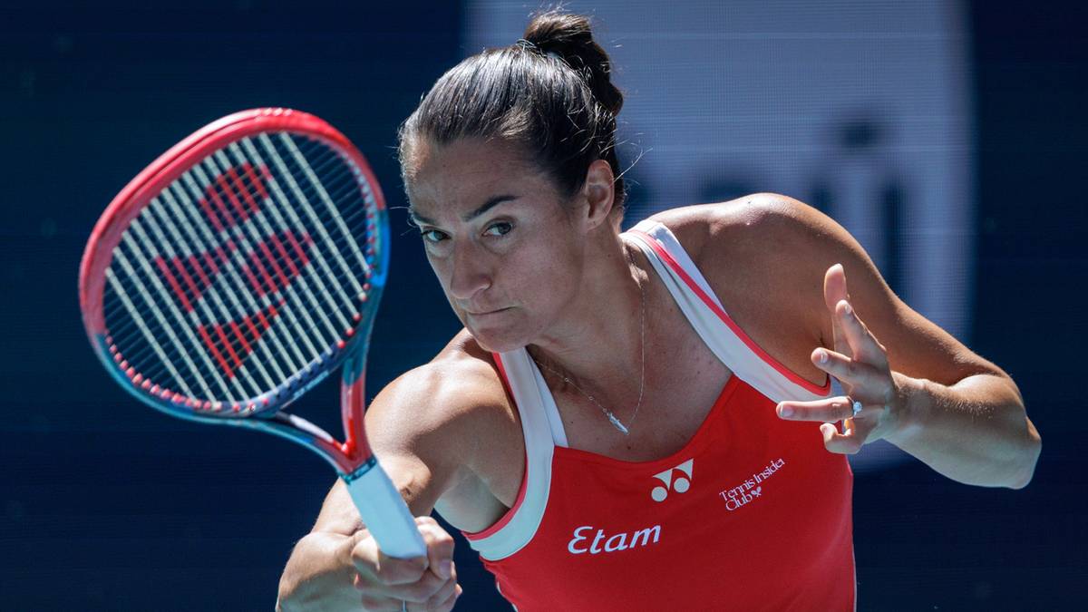 Kobieta tenisistka z rakietą w ręku, skupiona na grze, w czerwonej koszulce sportowej.