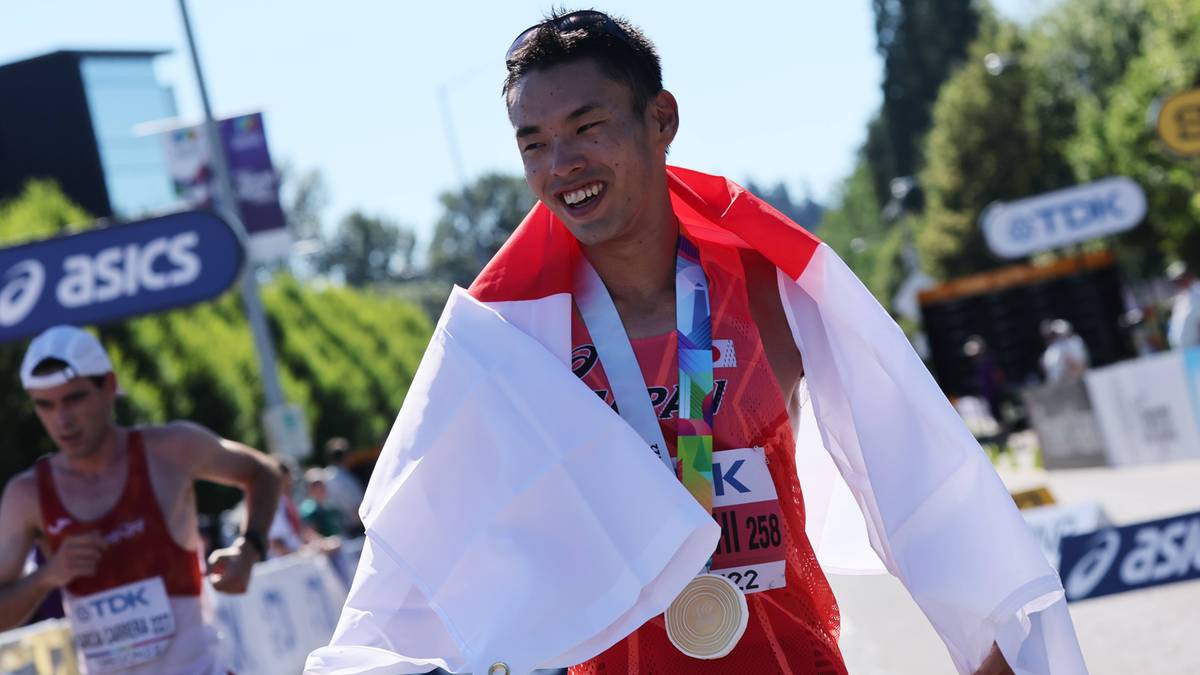 Szczęśliwy Japończyk w czerwonej koszulce sportowej, z medalem na szyi i biało-czerwoną flagą narzuconą na ramiona, podczas zawodów sportowych.