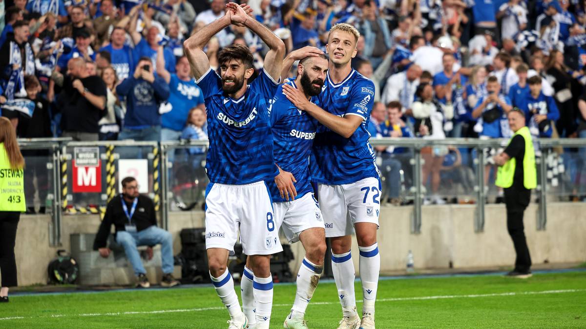 Trzech piłkarzy w niebiesko-białych strojach celebruje zdobycie bramki.