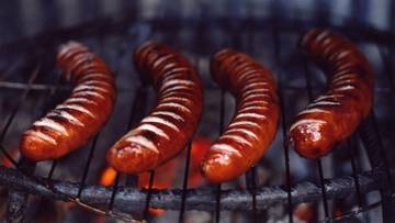 Cztery kiełbaski smażone na ruszcie nad żarem.