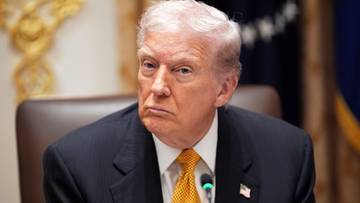 Donald Trump w garniturze i żółtym krawacie, siedzący przy stole.