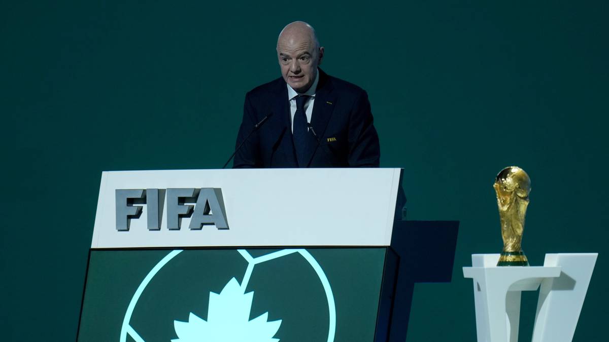 Gianni Infantino podczas Kongresu FIFA stoi przy m&oacute;wnicy z logo FIFA i pucharem świata.