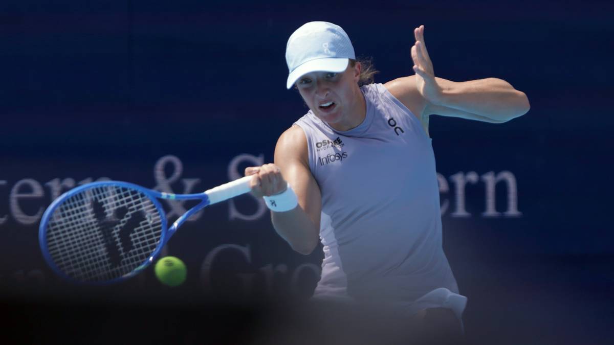 Iga Świątek odbija piłkę do tenisa podczas meczu, ubrana jest w białą czapeczkę i niebieską koszulkę bez rękawów.