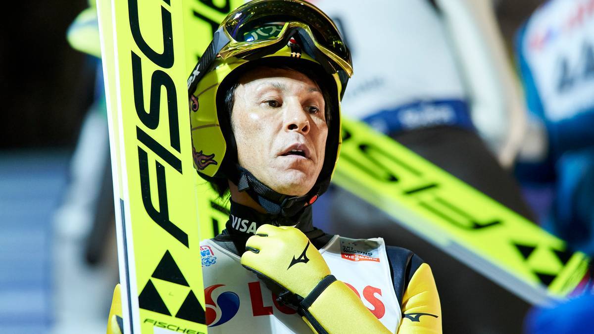 Skoczek narciarski Noriaki Kasai w kasku i goglach, trzymający nartę.