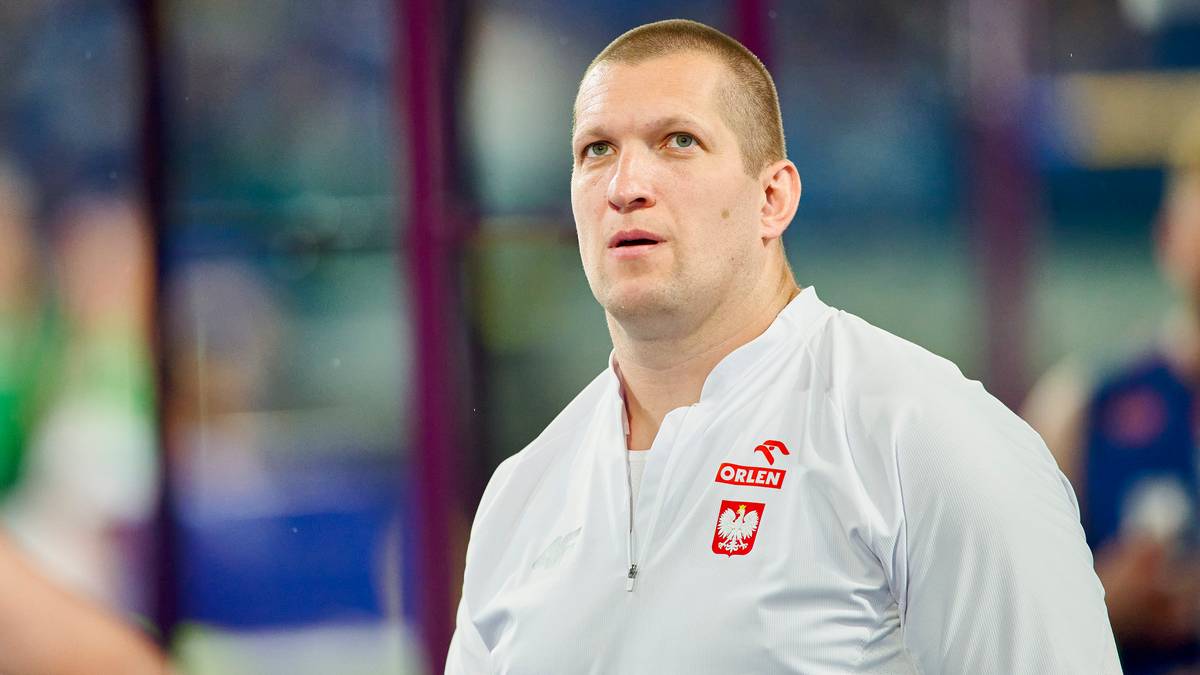 Portret polskiego sportowca w białej bluzie z godłem narodowym.