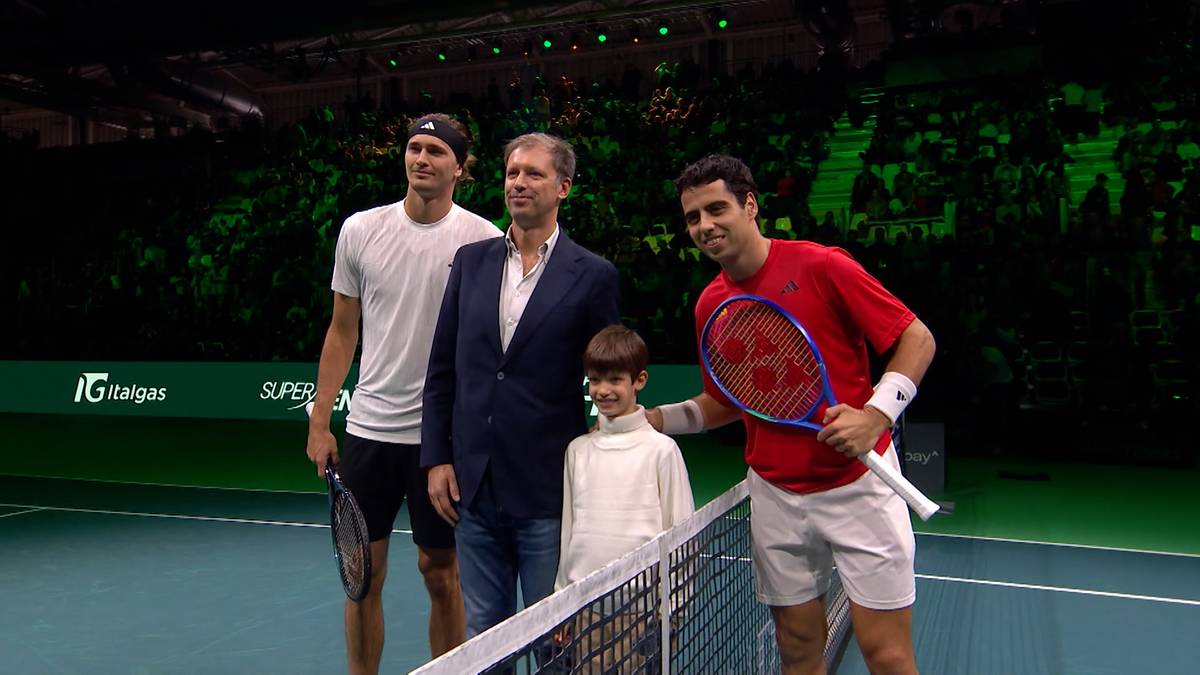 Czterech mężczyzn, w tym dwóch tenisistów z rakietami, stoi na korcie tenisowym.