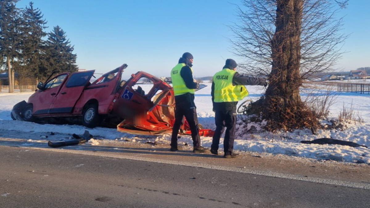 Rozbity czerwony bus po wypadku drogowym, obok policjanci prowadzący czynności