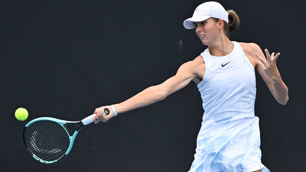 Kobieta w białym stroju tenisowym uderza piłkę rakietą.