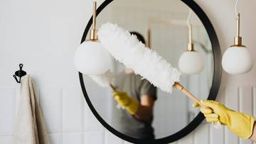 Osoba w żółtych rękawiczkach przeciera lusterko białą, puszystą ściereczką.