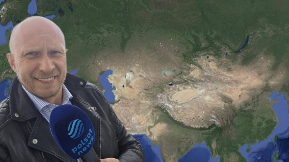 Uśmiechnięty mężczyzna z łysą głową, trzymający mikrofon Polsat News na tle mapy Azji.