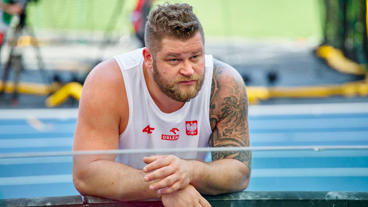 Paweł Fajdek, polski lekkoatleta, miotacz, oparty o bandę na stadionie.