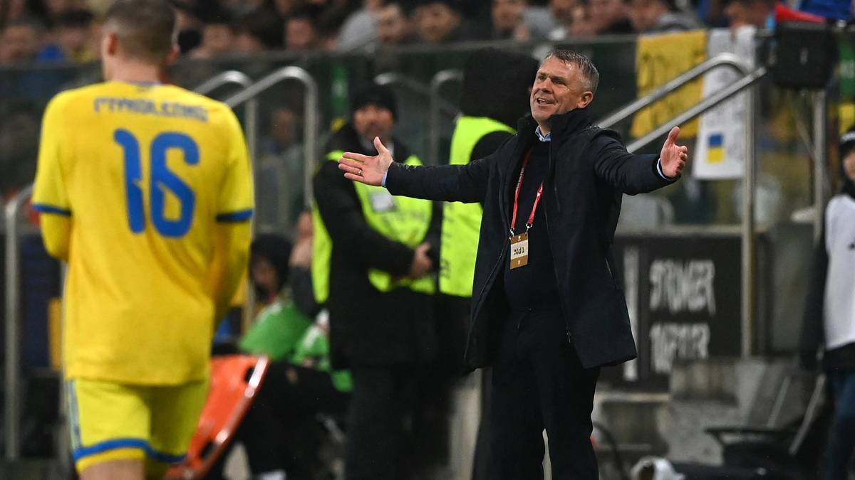 Trener piłkarski gestykuluje do zawodnika w żółtej koszulce z numerem 16.