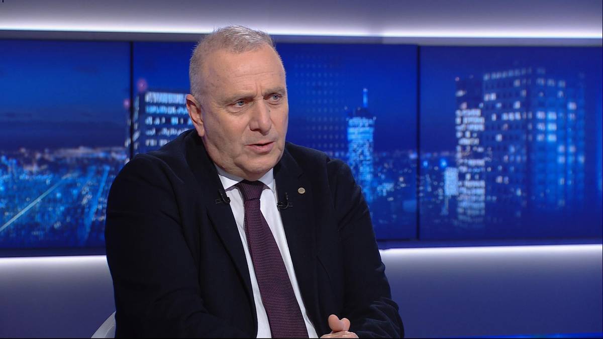 Mężczyzna w garniturze siedzący przed ekranami z widokiem nocnego miasta.