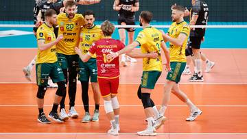 Drużyna siatkarzy w ż&oacute;łto-zielonych strojach świętuje na boisku, jeden zawodnik w czerwonej koszulce stoi pośrodku.