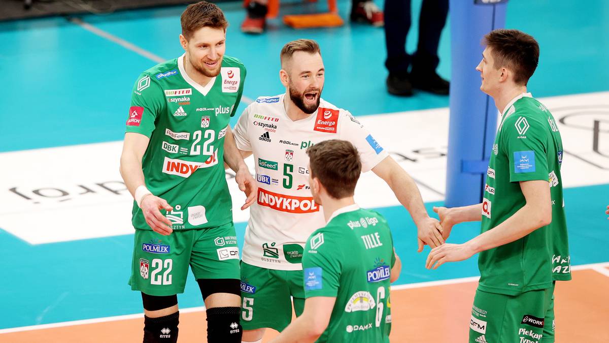 Siatkarze w zielonych strojach świętujący na boisku, jeden z nich wykonuje gest z zawodnikiem w białej koszulce.